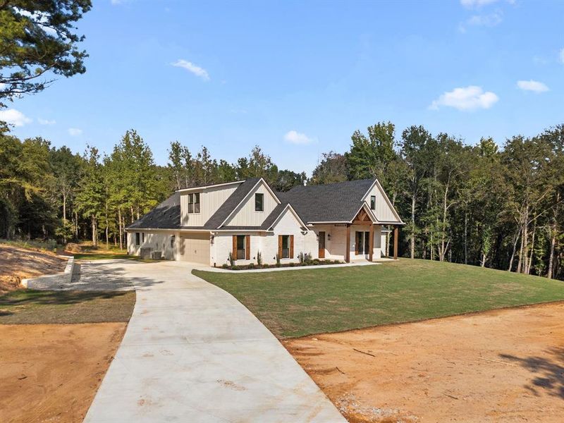 Modern farmhouse featuring concrete driveway, a garage, a porch, board and batten siding, and a front yard