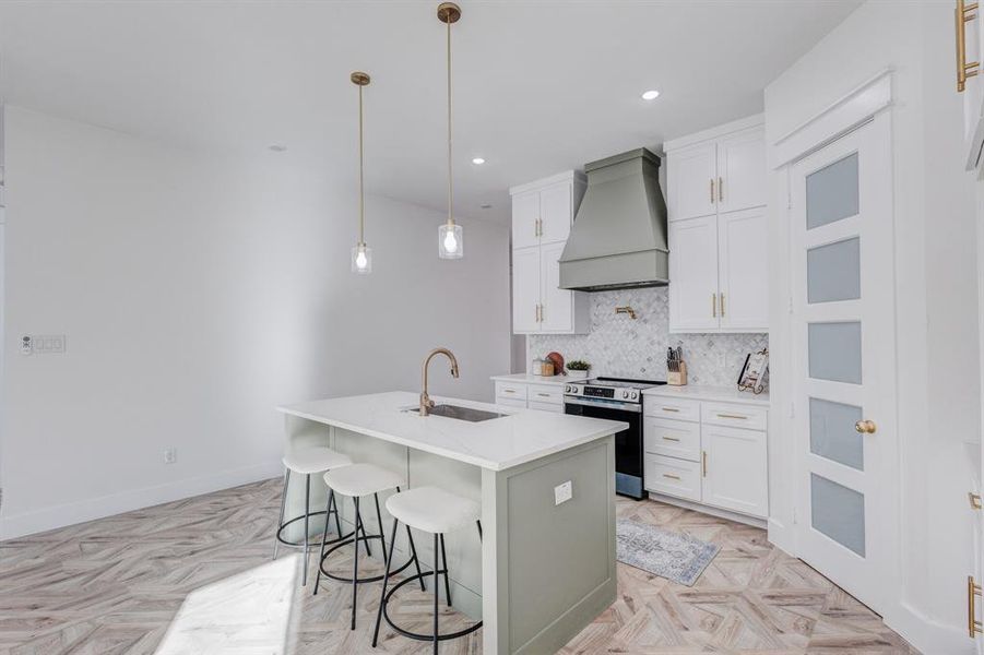 Kitchen with electric range, sink, pendant lighting, a kitchen island with sink, and custom exhaust hood