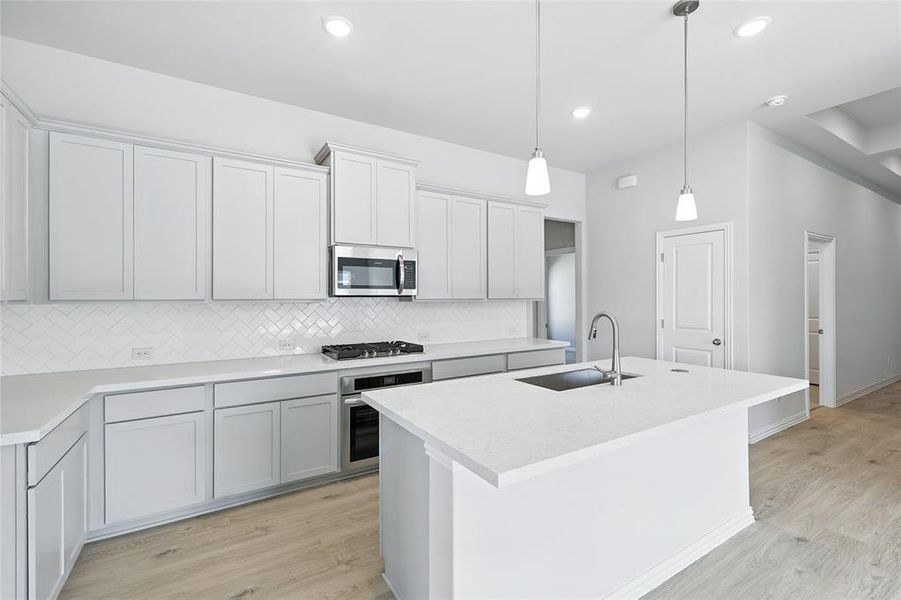 Kitchen with appliances with stainless steel finishes, light wood finished floors, a kitchen island with sink, decorative light fixtures, and recessed lighting Kitchen with appliances with stainless steel finishes, light wood finished floors, a kitchen island with sink, decorative light fixtures, and recessed lighting