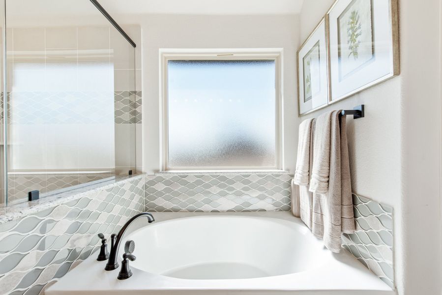 Soaking tub with black faucet, decorative tile surround, frosted window, and towel bar with folded towels Soaking tub with black faucet, decorative tile surround, frosted window, and towel bar with folded towels