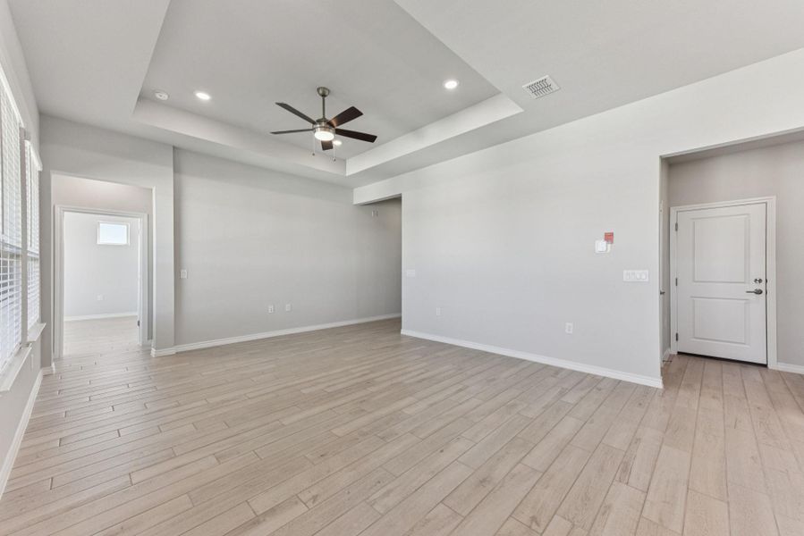 Empty room featuring a raised ceiling, light wood-style flooring, ceiling fan, and recessed lighting Empty room featuring a raised ceiling, light wood-style flooring, ceiling fan, and recessed lighting