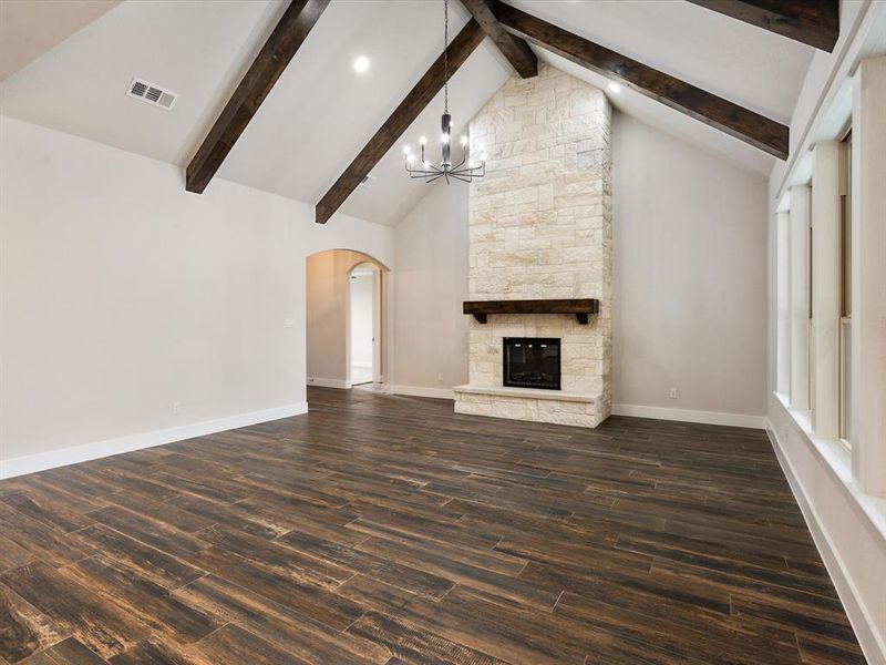 Unfurnished living room with a notable chandelier, beam ceiling, a fireplace, and dark hardwood / wood-style flooring