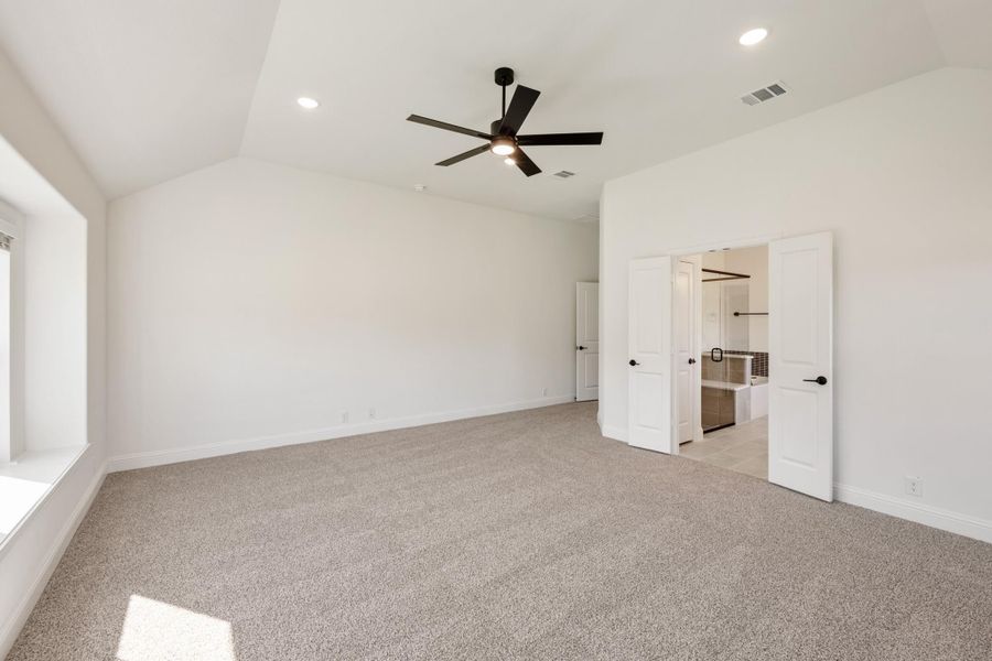 Empty master bedroom with vaulted ceiling, ceiling fan, carpet flooring, and open ensuite bathroom door Empty master bedroom with vaulted ceiling, ceiling fan, carpet flooring, and open ensuite bathroom door