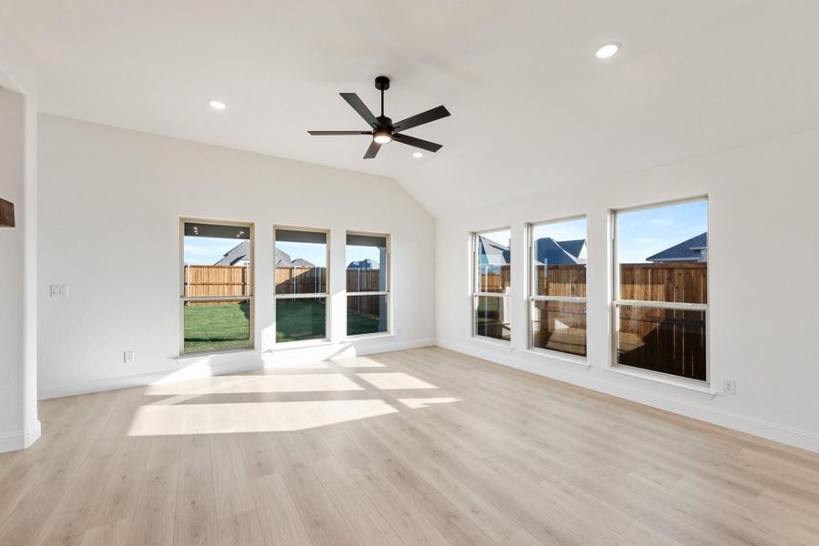Empty living room with vaulted ceiling, ceiling fan, light wood floors, and large windows overlooking backyard Empty living room with vaulted ceiling, ceiling fan, light wood floors, and large windows overlooking backyard