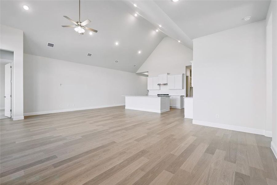 Unfurnished living room featuring a high ceiling, a ceiling fan, light wood finished floors, and recessed lighting