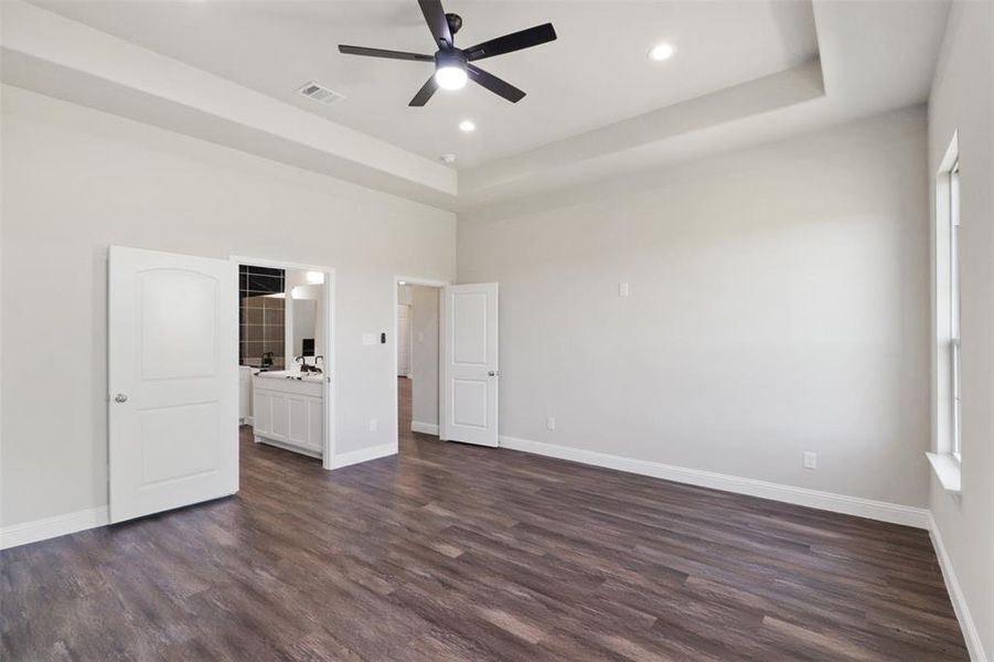 Unfurnished bedroom with a raised ceiling, ceiling fan, dark hardwood / wood-style flooring, and ensuite bath