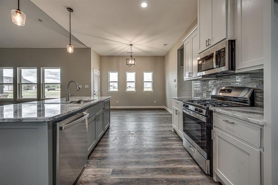 Kitchen with dark hardwood / wood-style flooring, a kitchen island with sink, appliances with stainless steel finishes, backsplash, and decorative light fixtures