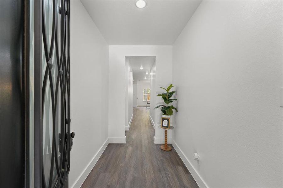 Entryway featuring a dark metal door with decorative ironwork, white walls, wood-finish flooring, recessed lighting, and white baseboards Entryway featuring a dark metal door with decorative ironwork, white walls, wood-finish flooring, recessed lighting, and white baseboards