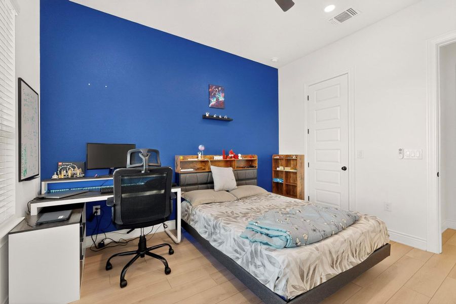 Bedroom featuring wood finished floors, a closet, a desk, a ceiling fan, and an accent wall