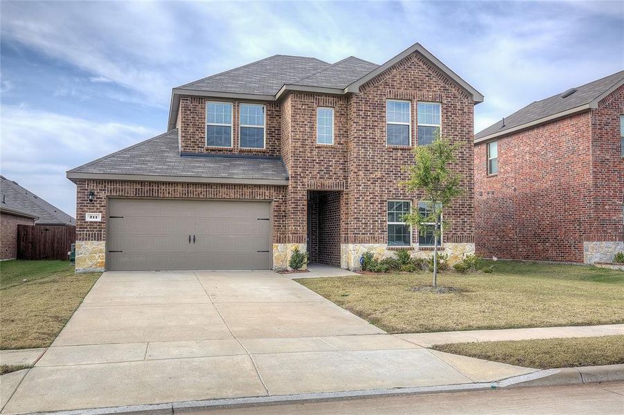 View of front of home with a shingled roof, stone siding, a front yard, and driveway