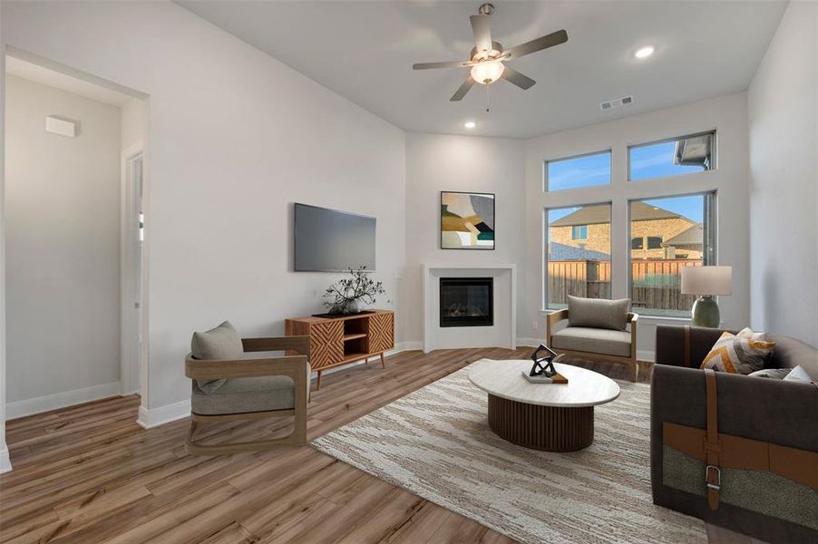Living area with ceiling fan, a glass covered fireplace, light wood-style floors, recessed lighting, and a high ceiling