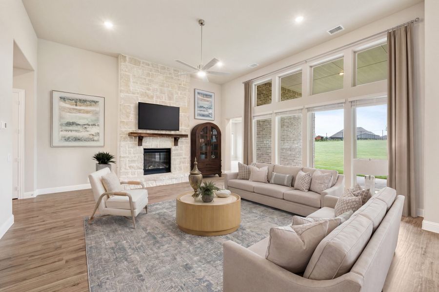 Living room with stone fireplace, neutral sofas, hardwood floors, and large windows overlooking a backyard.