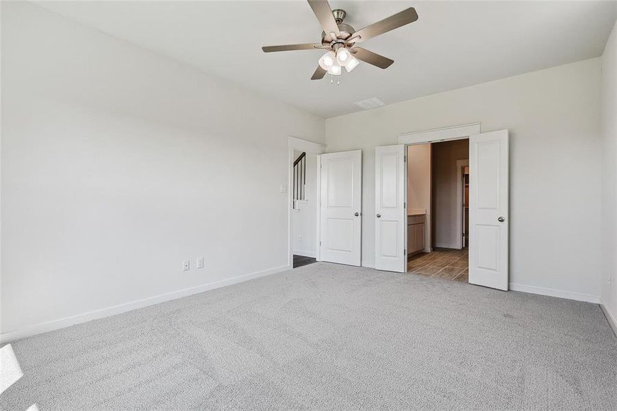 Unfurnished bedroom featuring ceiling fan, connected bathroom, and light colored carpet