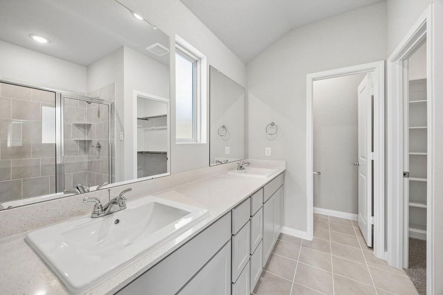A well-appointed primary bathroom showcases dual vanity sinks, a spacious glass-enclosed shower, and convenient walk-in closets.