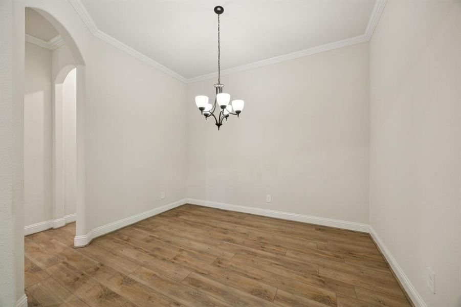 Dining room with luxury vinyl plank floors, ornamental molding, arched walkways, and a chandelier.