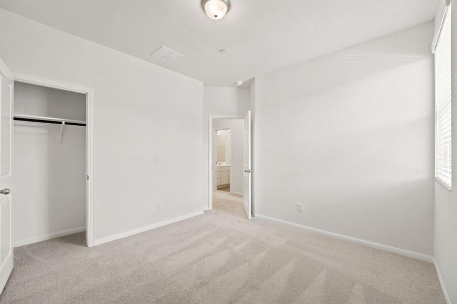 Soft carpeting underfoot and a large window define this comfortable, light-filled bedroom.