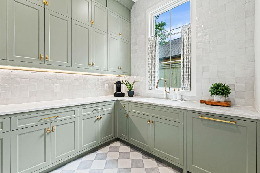 Another view highlighting the scullery kitchen’s refined finishes & thoughtful details. A window above the sink w/ custom café curtains brings in natural light, while the patterned porcelain tile flooring adds a subtle design statement. A beautifully finished space designed to support both prep & organization behind the scenes. Another view highlighting the scullery kitchen’s refined finishes & thoughtful details. A window above the sink w/ custom café curtains brings in natural light, while the patterned porcelain tile flooring adds a subtle design statement. A beautifully finished space designed to support both prep & organization behind the scenes.