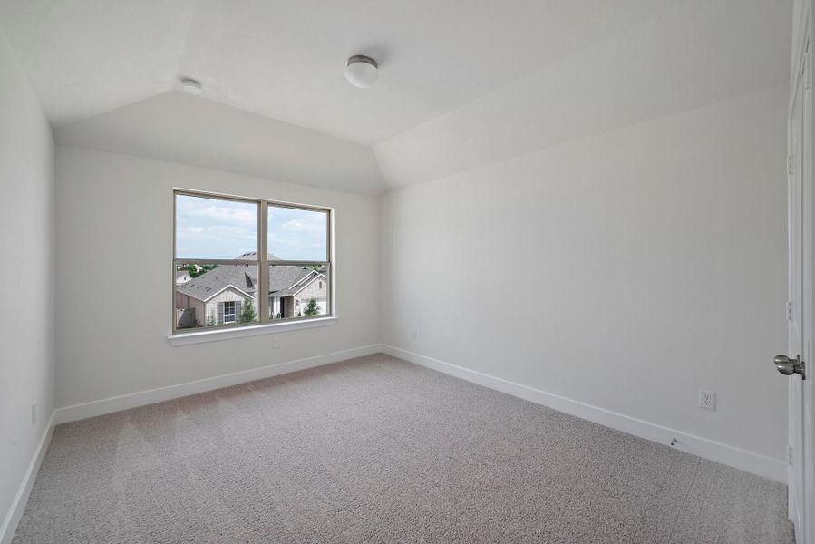 Empty room with vaulted ceiling and light carpet
