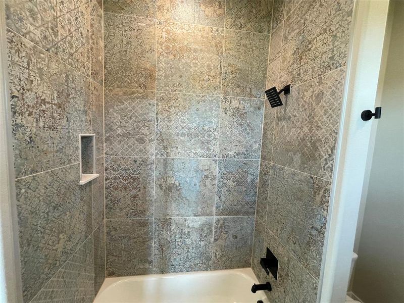 Bathtub shower combination featuring patterned wall tile, a built-in shower niche with shelf, and matte black fixtures