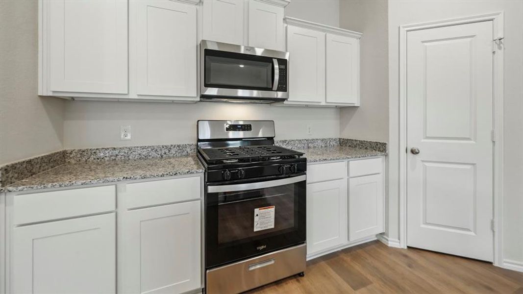 Kitchen featuring white shaker cabinetry, stainless steel appliances, granite countertops, and wood-finish flooring