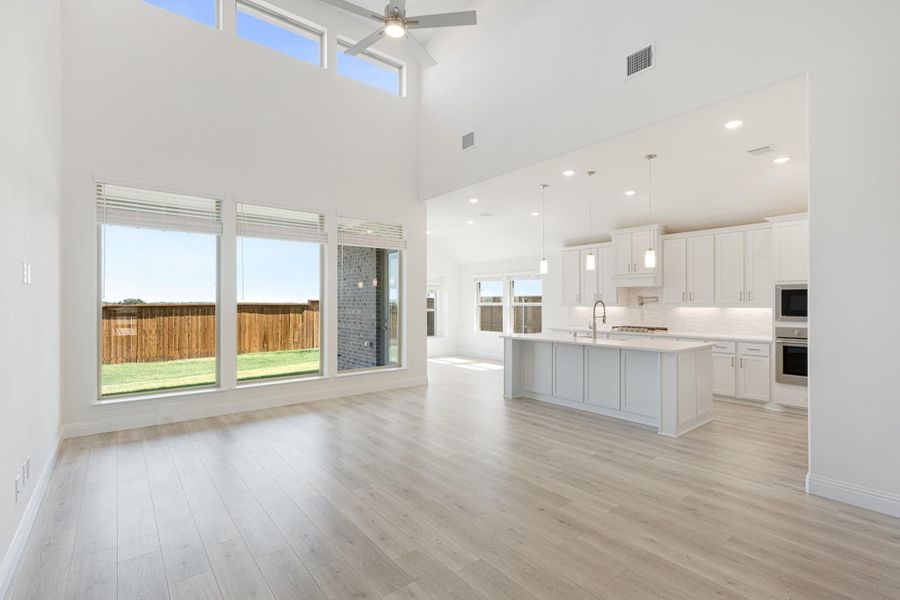 Open-concept living area with high ceilings, light wood floors, and white kitchen with island and pendant lights Open-concept living area with high ceilings, light wood floors, and white kitchen with island and pendant lights