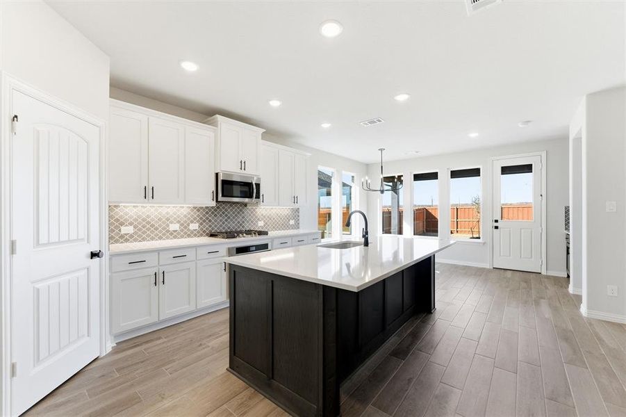 Kitchen featuring white cabinets, light wood finished floors, a kitchen island with sink, decorative light fixtures, and recessed lighting