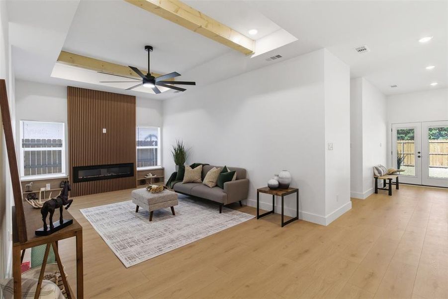 Spacious living area featuring light wood-finish flooring, a contemporary fireplace with a slatted wood accent wall, and a tray ceiling with exposed wood beams