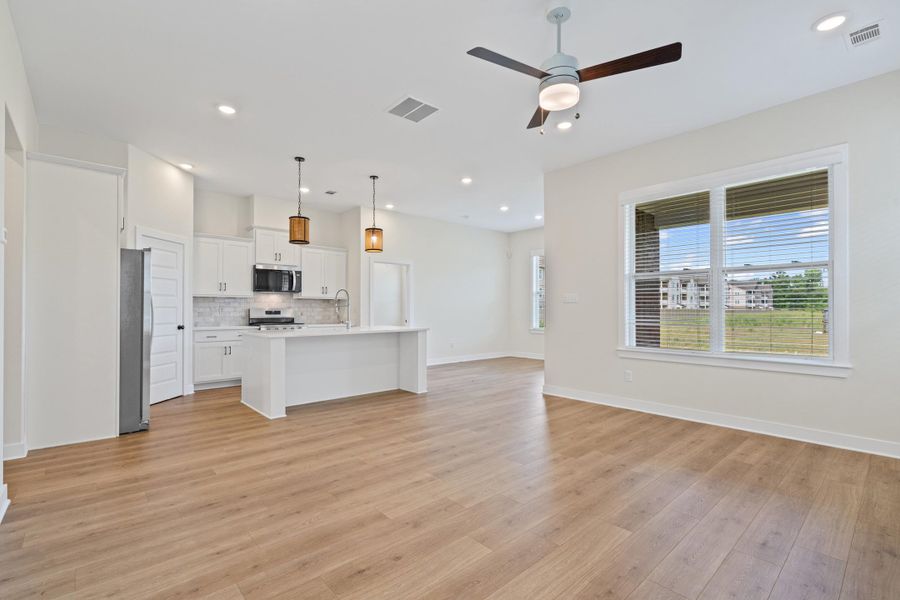 Open-concept interior featuring wood-finish flooring, a white kitchen island, and stainless steel appliances Open-concept interior featuring wood-finish flooring, a white kitchen island, and stainless steel appliances