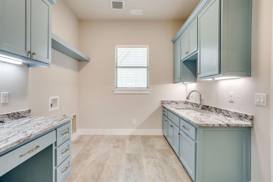 Utility room featuring light blue cabinetry, mottled stone-finish countertops, undermount sink with gooseneck faucet, under-cabinet lighting, and wood-finish flooring