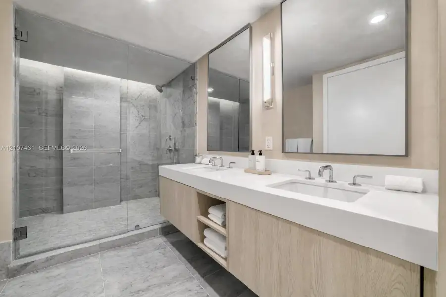 Floating dual vanity with integrated countertop, walk-in shower featuring glass enclosure and stone-tile surrounds, and rectangular wall-mounted mirrors Floating dual vanity with integrated countertop, walk-in shower featuring glass enclosure and stone-tile surrounds, and rectangular wall-mounted mirrors