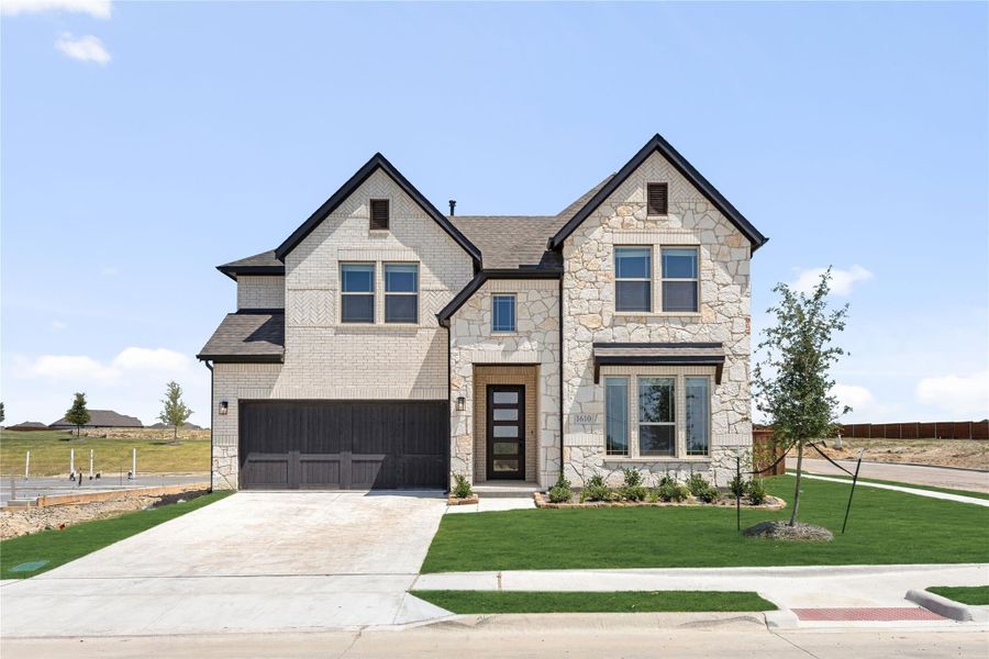 Two-story home with cream brick and stone exterior, dark two-car garage, and manicured front lawn