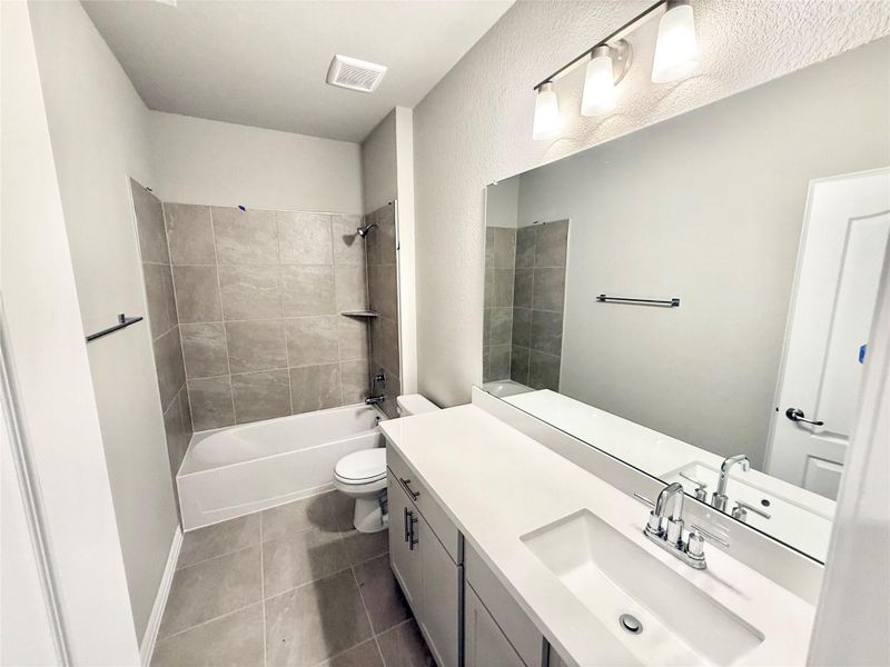 Full bath featuring vanity, bathing tub / shower combination, and dark tile patterned flooring Full bath featuring vanity, bathing tub / shower combination, and dark tile patterned flooring