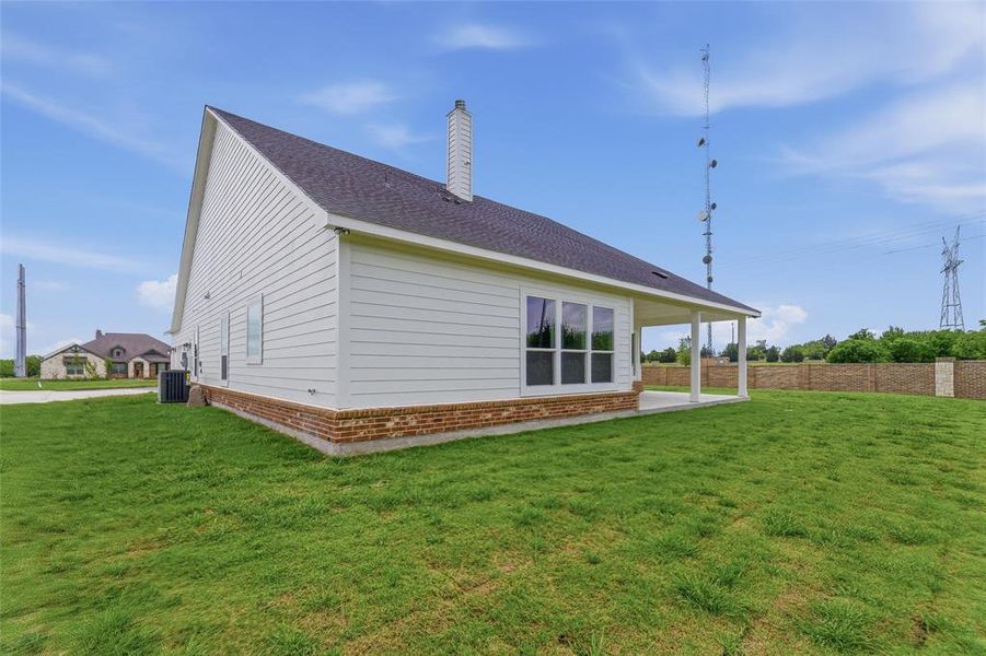 The property features white siding, a dark roof, and a brick foundation, with a covered patio area and an expansive lawn