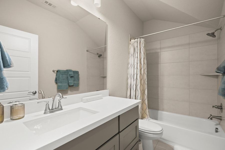 Bathroom featuring vanity, shower / bath combo, vaulted ceiling, and light tile patterned floors Bathroom featuring vanity, shower / bath combo, vaulted ceiling, and light tile patterned floors