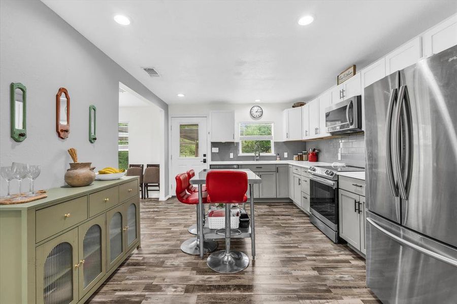 Kitchen with stainless steel appliances, backsplash, light countertops, dark wood-style flooring, and recessed lighting