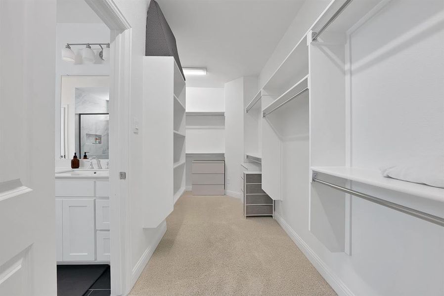 Walk-in closet with extensive built-in shelving, hanging rods, central storage island with drawers, and neutral carpeting