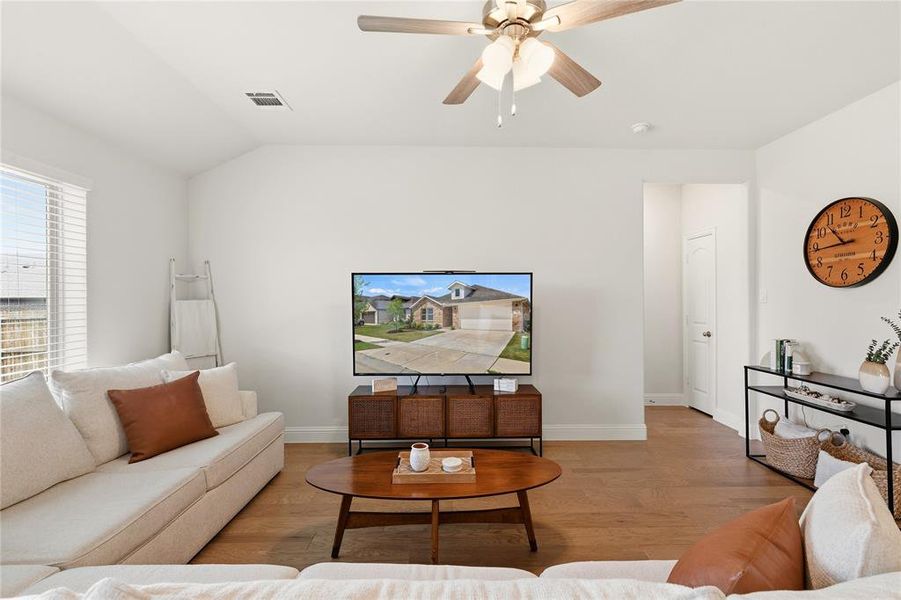 Spacious living area featuring wood-finish flooring, a ceiling fan with light fixture, and a large window with blinds