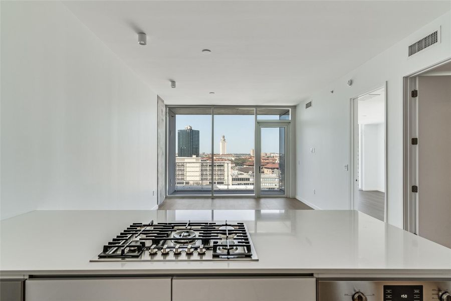 A sleek kitchen island with a gas range overlooks the cityscape through a vast window wall. A sleek kitchen island with a gas range overlooks the cityscape through a vast window wall.