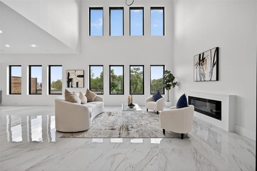 Living room with light marble finish floors, a high ceiling, and a glass covered fireplace
