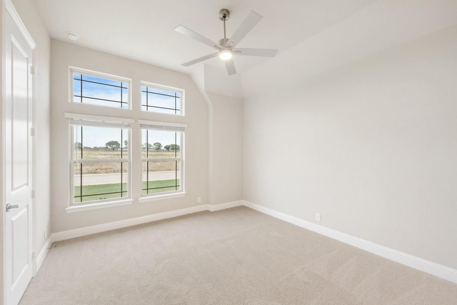 Empty bedroom with vaulted ceiling, ceiling fan, carpet flooring, and large windows with outdoor views