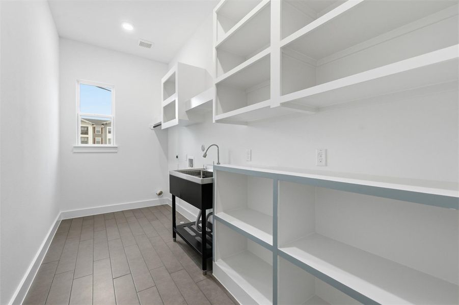 Laundry room features custom shelving, additional outlets, and an oversized utility sink. Tile flooring adds durability, while a window fills the space with natural light. Equipped with both gas and electric dryer connections for maximum flexibility.
