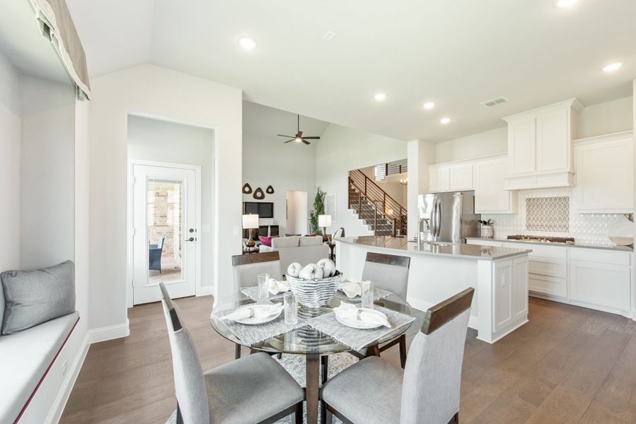 Open-concept dining area with glass table and four chairs, adjacent to white kitchen with island and stainless appliances Open-concept dining area with glass table and four chairs, adjacent to white kitchen with island and stainless appliances