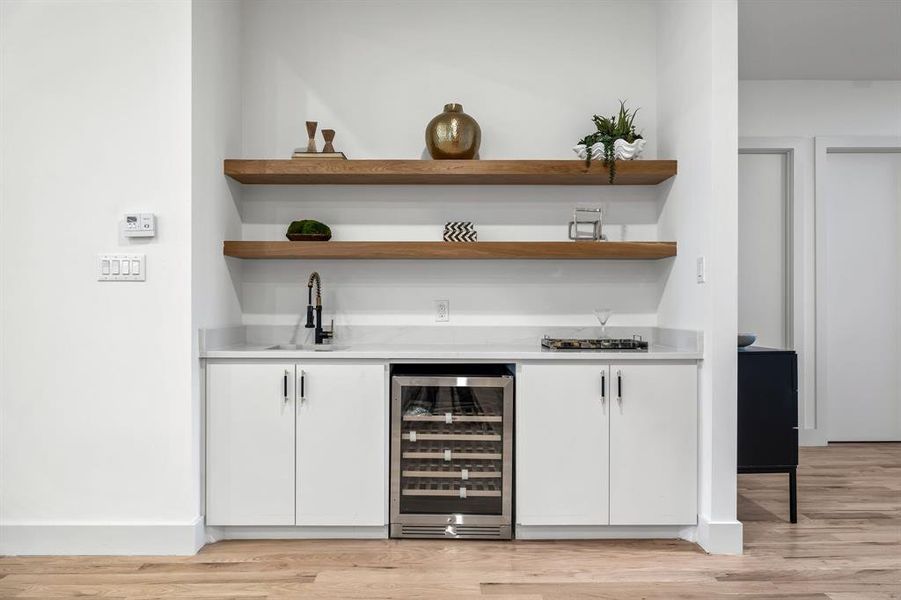 Bar with white cabinetry, sink, beverage cooler, and light wood-type flooring