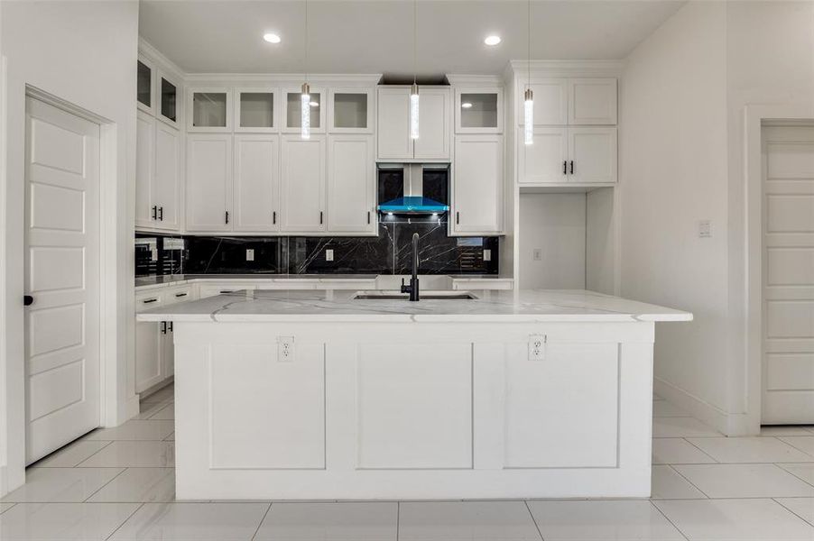Kitchen with backsplash, light stone countertops, white cabinets, glass insert cabinets, and ventilation hood