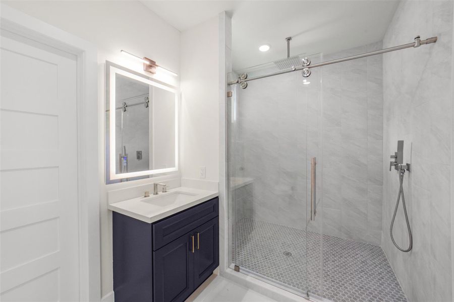 This modern bathroom features a sleek walk-in shower with glass doors and stylish tile work. It includes a chic vanity with a backlit mirror, providing a clean and elegant look.