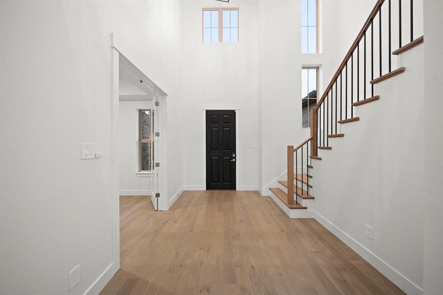 Foyer entrance with light wood-style floors, stairs, and a towering ceiling