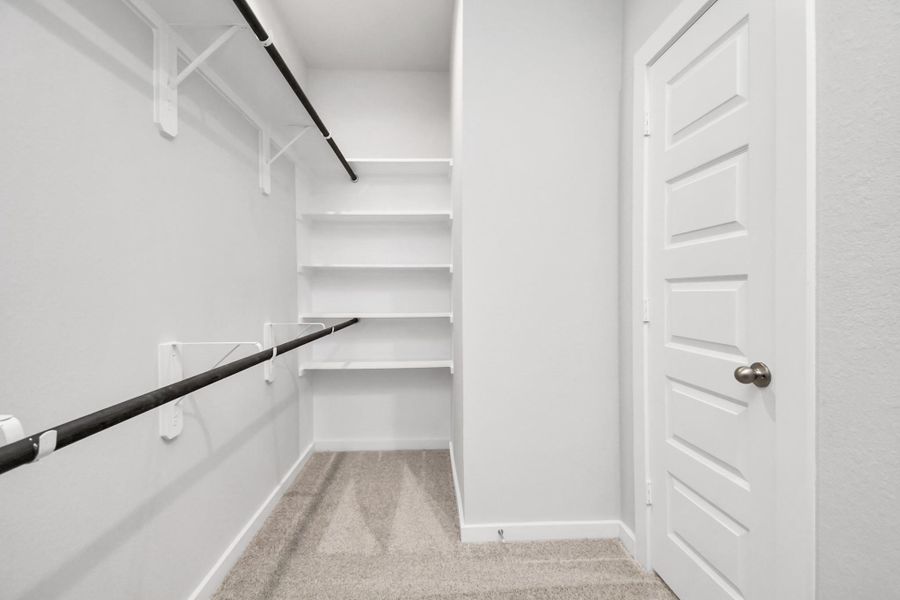 Step into a walk-in closet that defines luxury and functionality. This generously sized space boasts built-in shelving, providing ample room for organization. With high ceilings and recessed lighting, the ambiance is both bright and welcoming. Plush carpeting underfoot enhances the comfort, while warm paint tones add a touch of coziness. Sample photo of completed home with similar floor plan. As-built interior colors and selections may vary. Step into a walk-in closet that defines luxury and functionality. This generously sized space boasts built-in shelving, providing ample room for organization. With high ceilings and recessed lighting, the ambiance is both bright and welcoming. Plush carpeting underfoot enhances the comfort, while warm paint tones add a touch of coziness. Sample photo of completed home with similar floor plan. As-built interior colors and selections may vary.