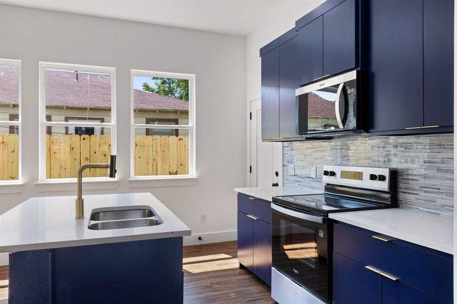 Kitchen with blue cabinets, stainless steel appliances, dark wood-style flooring, light stone counters, and modern cabinets