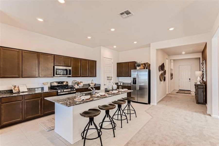 Kitchen featuring dark brown cabinets, a kitchen breakfast bar, dark stone counters, stainless steel appliances, and recessed lighting
