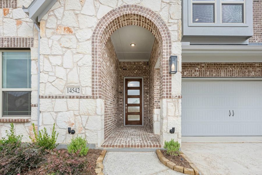 Home entrance with stone and brick arched entryway, wood front door with glass panels, and attached garage